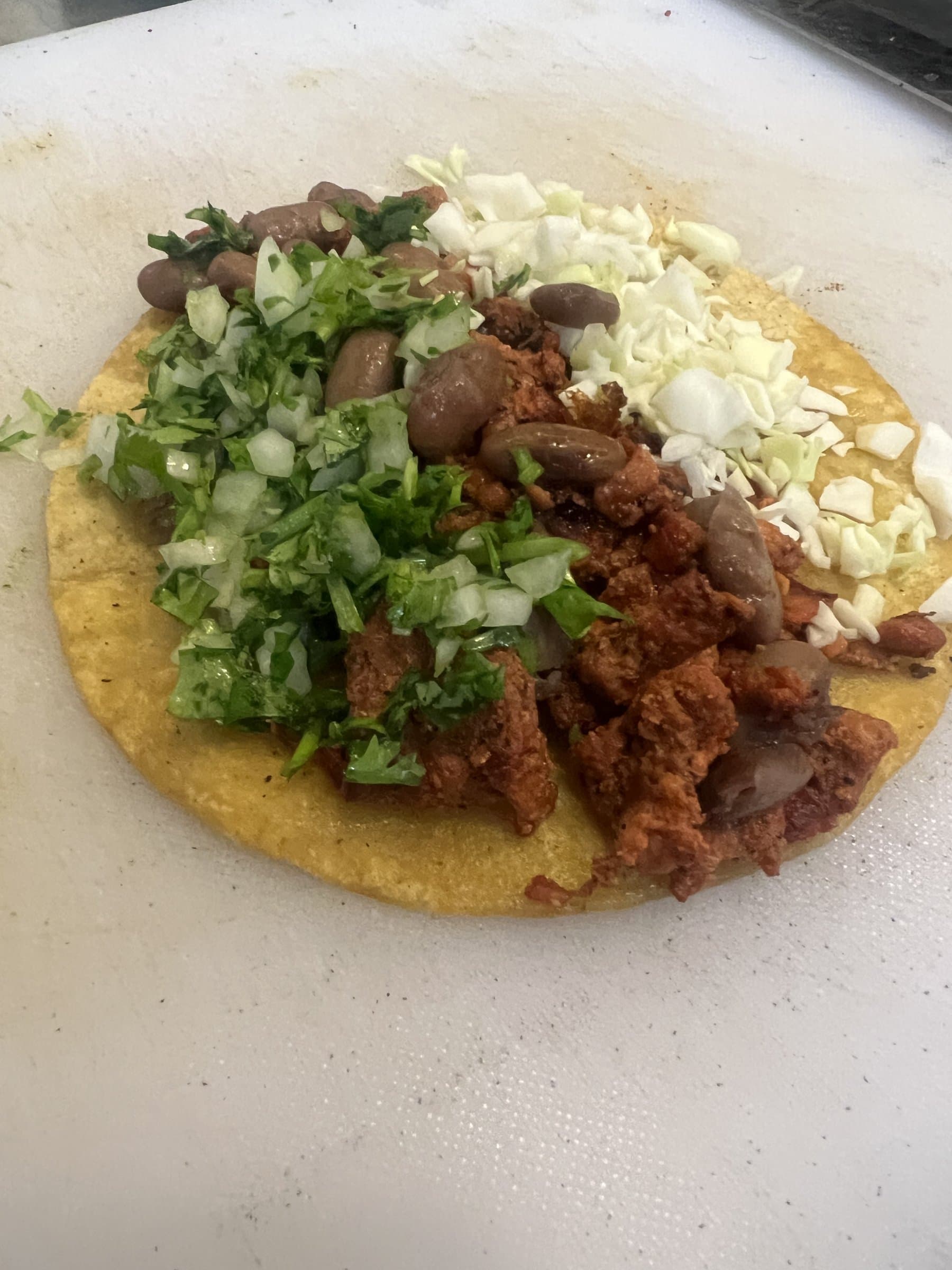 Al pastor taco being built with fresh cilantro, onion, cabbage, and beans